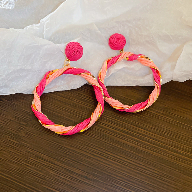 Twisted Contrast Grass Vine Earrings made of alloy and grass vine, featuring pink and orange hues on a wood surface.