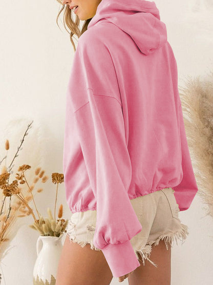 Pink zip-up dropped shoulder hoodie with pockets and drawstring, polyester-rayon blend, worn over frayed shorts.