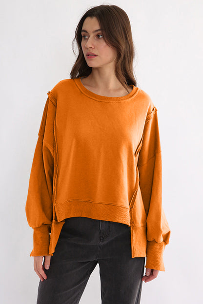 Exposed seam high-low sweatshirt in orange, featuring long sleeves and slit design.