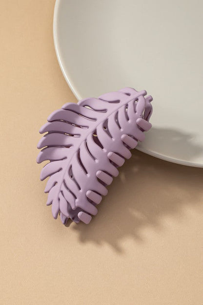 Feather-shaped purple hair claw clip with matte finish on tan background.