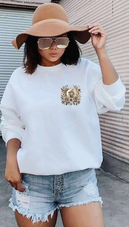 Woman wearing a Time to Shine Graphic Sweatshirt with embroidered floral design, paired with denim shorts and a wide-brimmed hat.