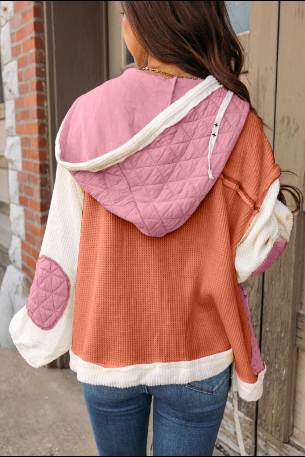 Long sleeve hooded jacket with drawstring, button-up design, exposed seams, and quilted details in pink and rust colors.