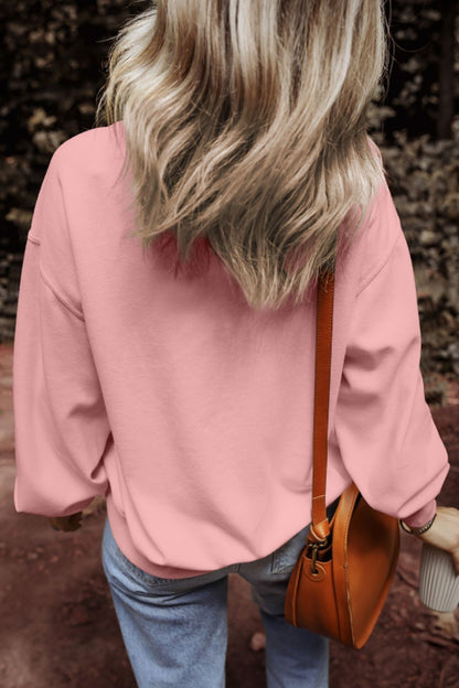 Round neck long sleeve sweatshirt in pink, worn by woman with wavy hair, paired with blue jeans and brown bag.