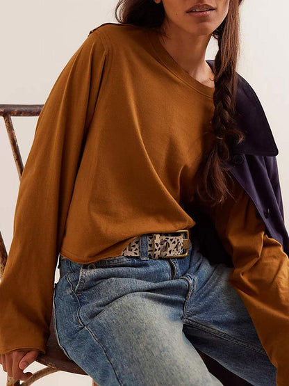 Round neck long sleeve cropped tee on woman, paired with jeans and a patterned belt.