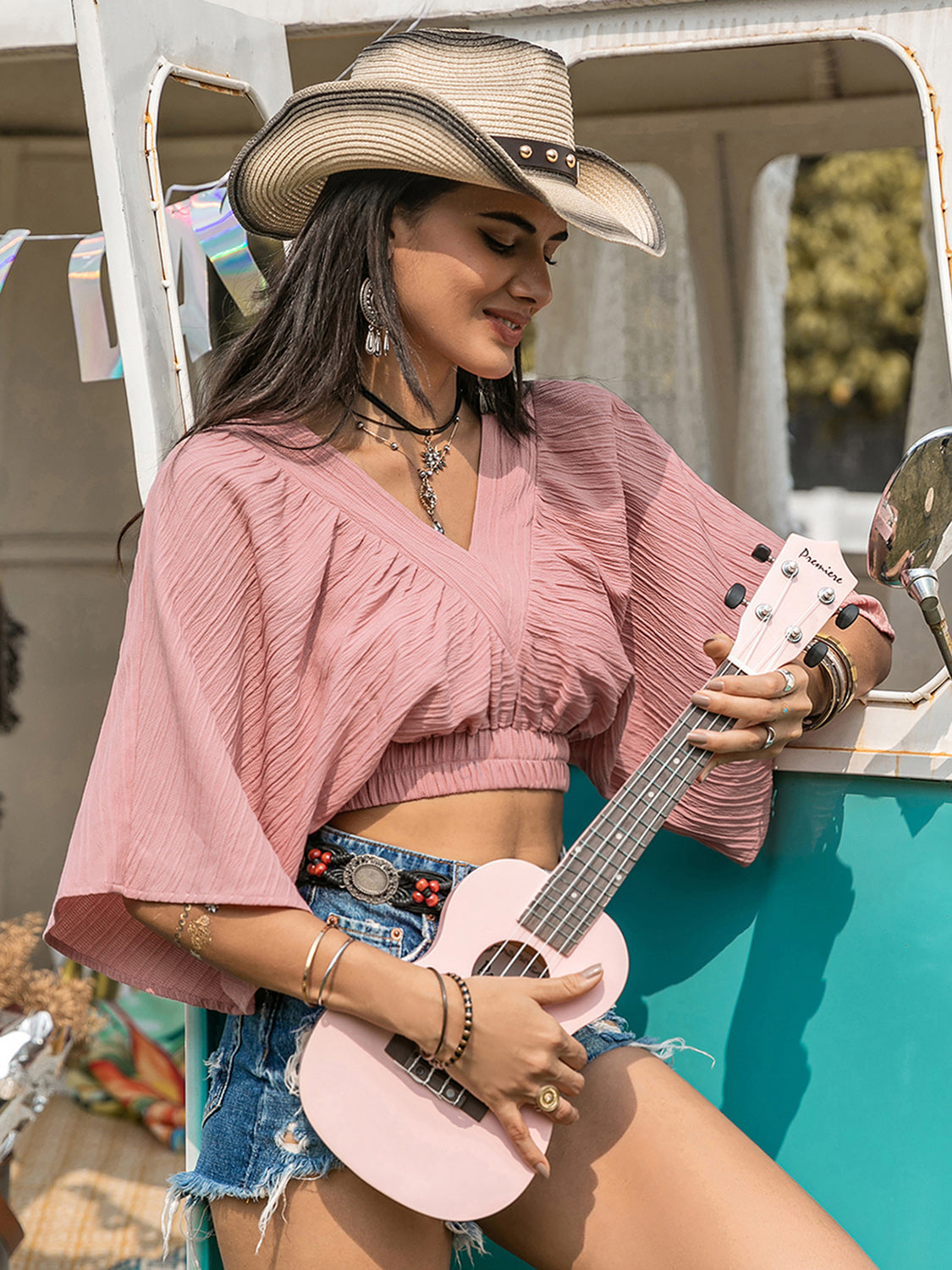 Boho crop top with ruched textured V-neck design in pink, styled with denim shorts and accessories.