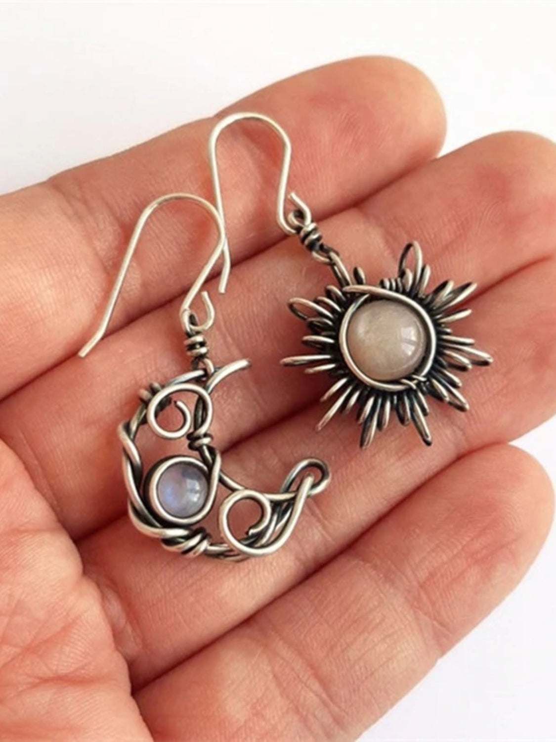 Moon & Sun dangle earrings featuring moonstone and alloy design on a hand.