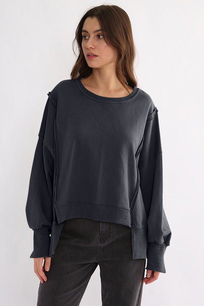 Exposed seam high-low long sleeve sweatshirt in black, slightly stretchy, 100% cotton, worn by a woman.