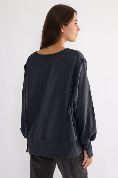 Exposed seam high-low long sleeve sweatshirt in dark color, featuring a slightly stretchy, opaque cotton material.