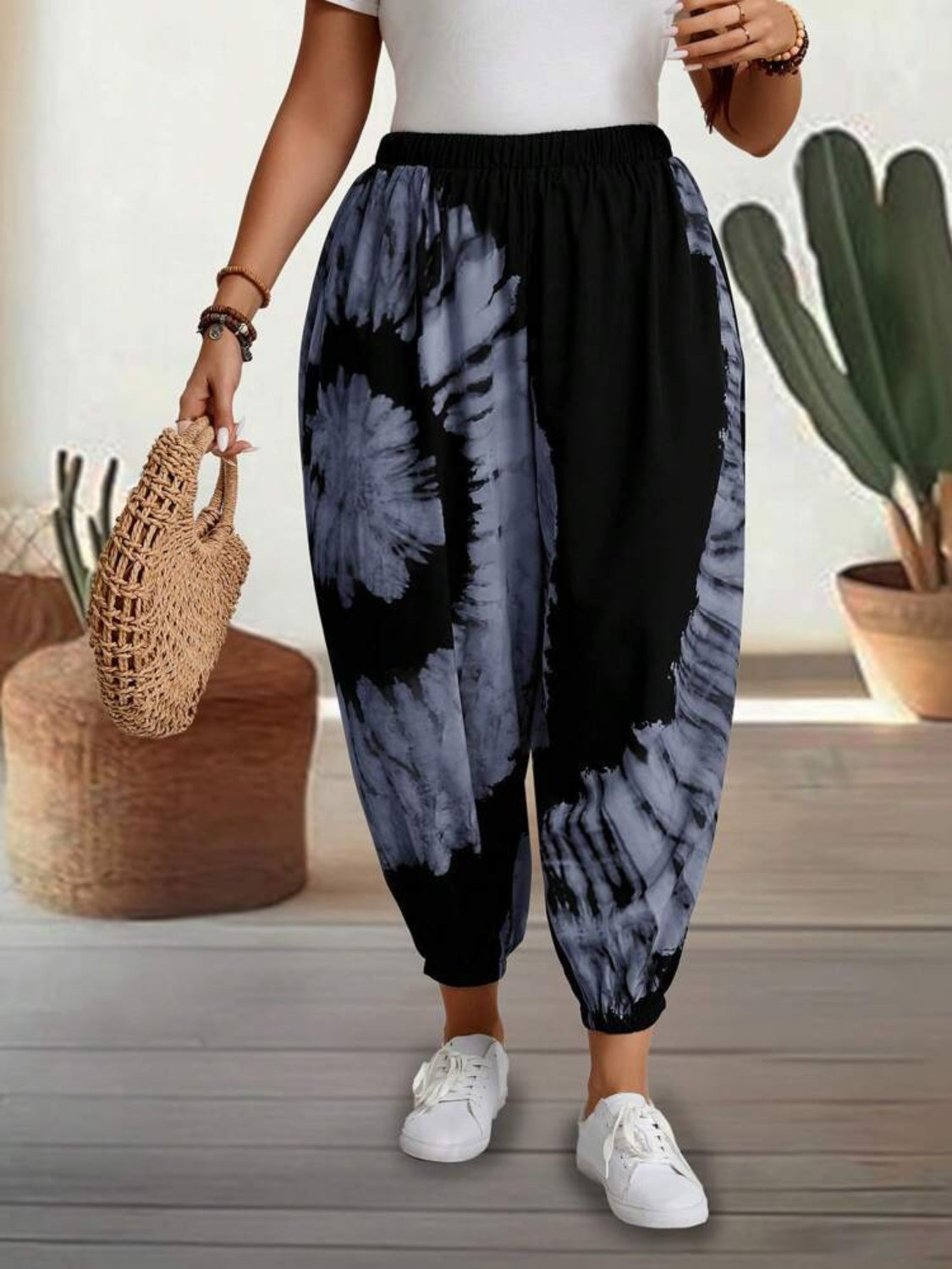 Tie-dye elastic waist pants in black and grey, worn by a person with a white top and white sneakers, carrying a woven bag.