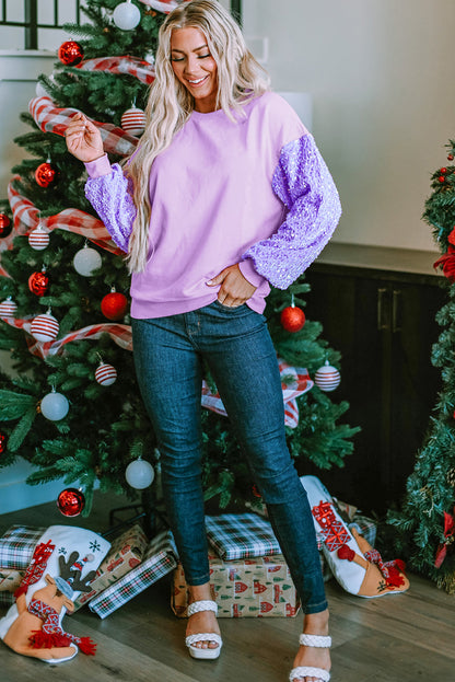 Sequin round neck long sleeve sweatshirt with purple sequin sleeves worn by woman in holiday setting.