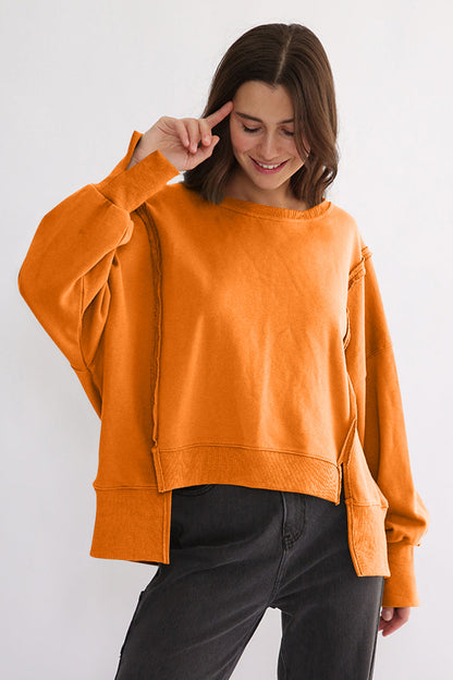 Exposed seam high-low orange sweatshirt with long sleeves and side slit.