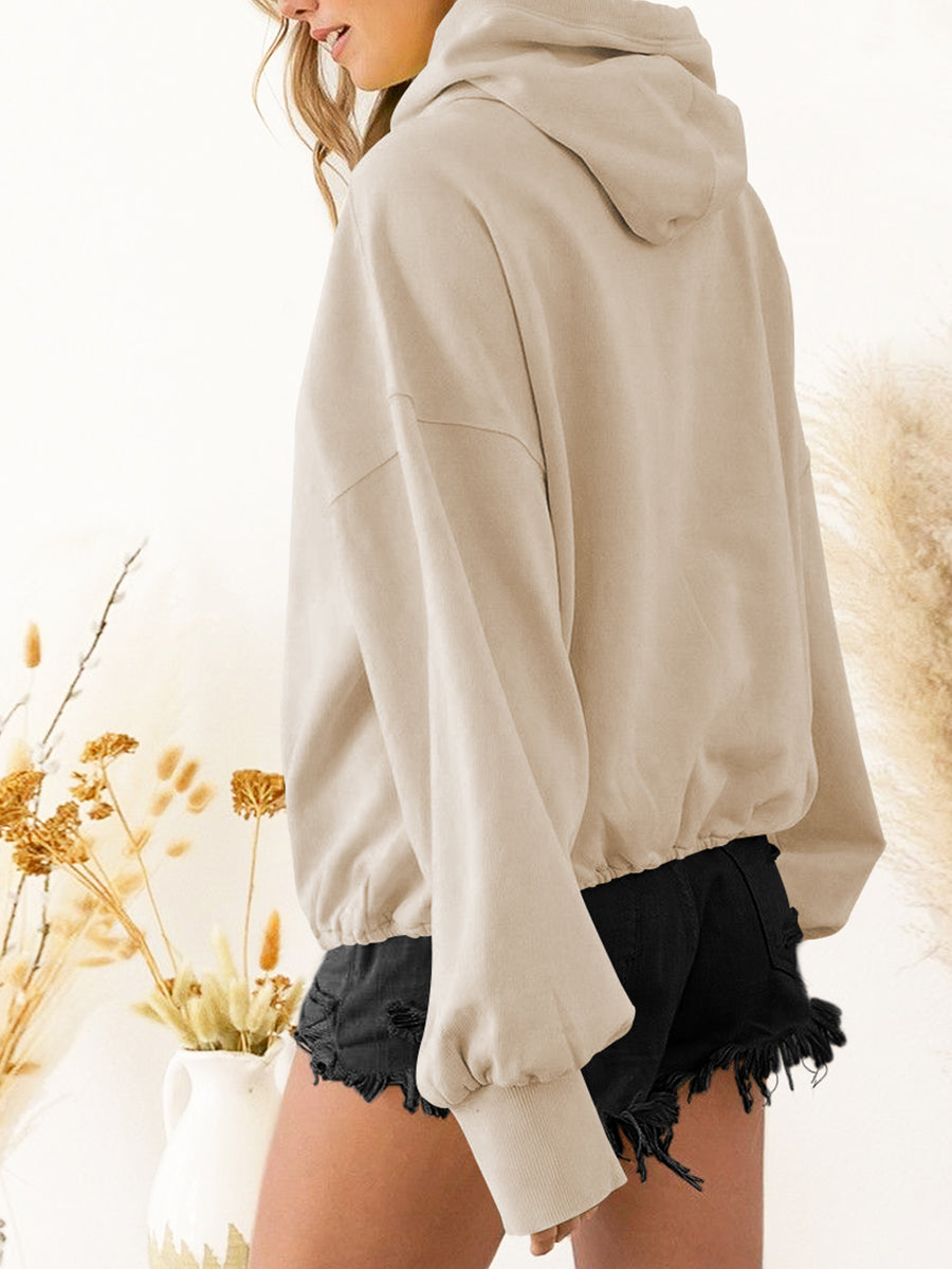 Beige zip-up dropped shoulder hoodie with pocket and drawstring, paired with black shorts.