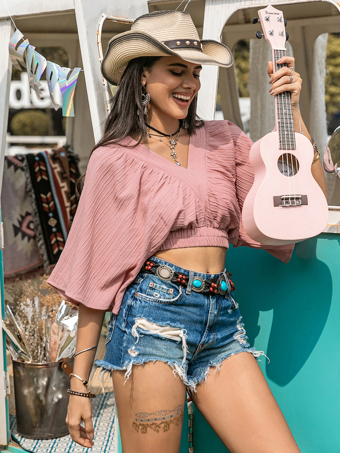 Boho crop top with textured V-neck design, 100% polyester, styled with distressed denim shorts and a hat.