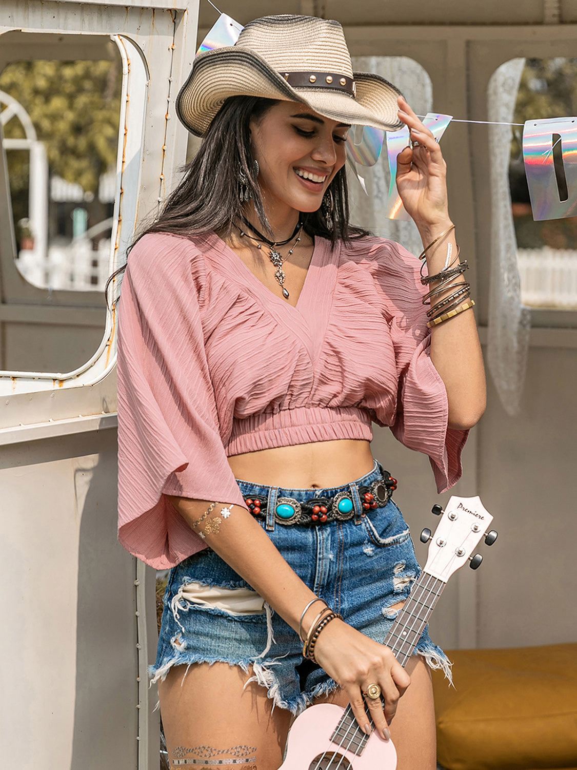 Boho crop top with textured V-neck and ruched details, worn by a woman in denim shorts and a cowboy hat.