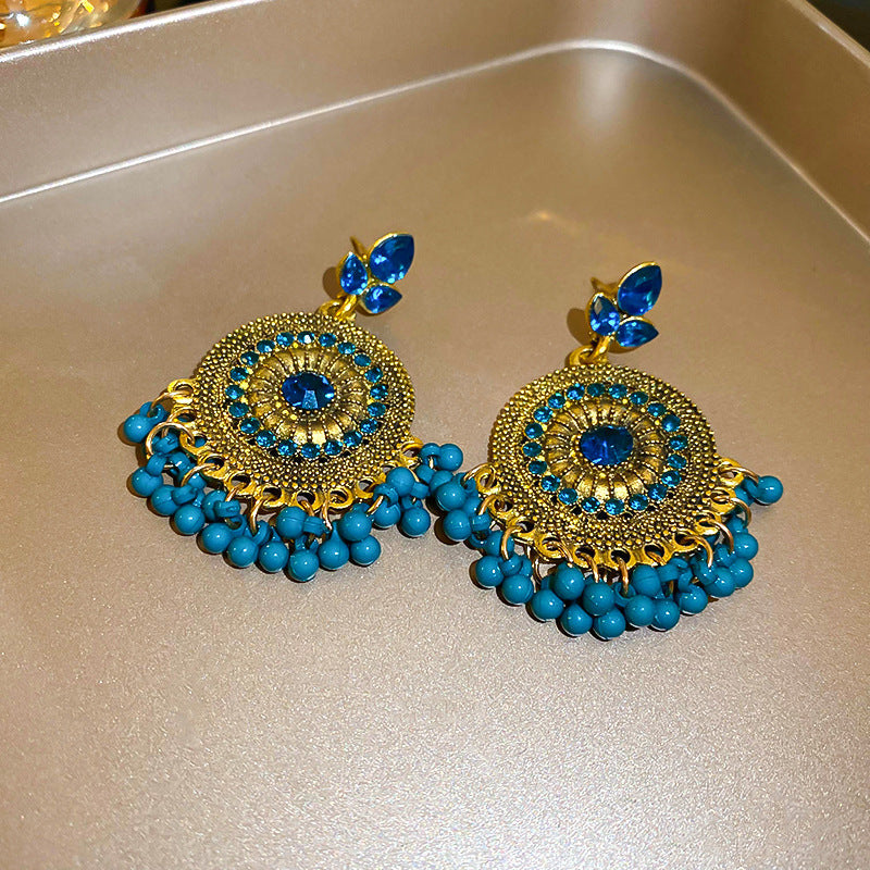 Rhinestone alloy bead dangle earrings with blue accents on a gold background.