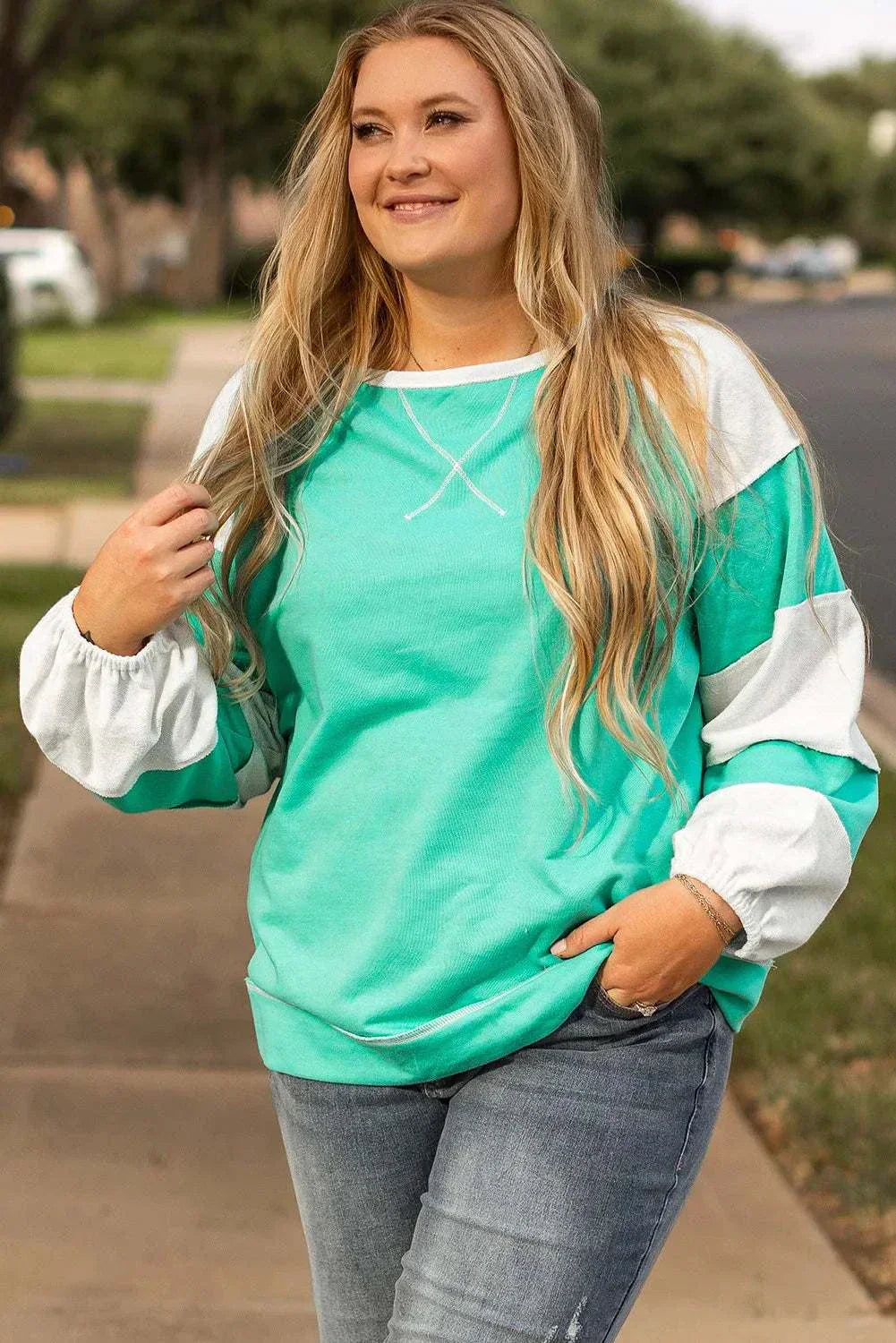 Plus size exposed seam color block long sleeve sweatshirt in green and white worn by a woman outdoors.