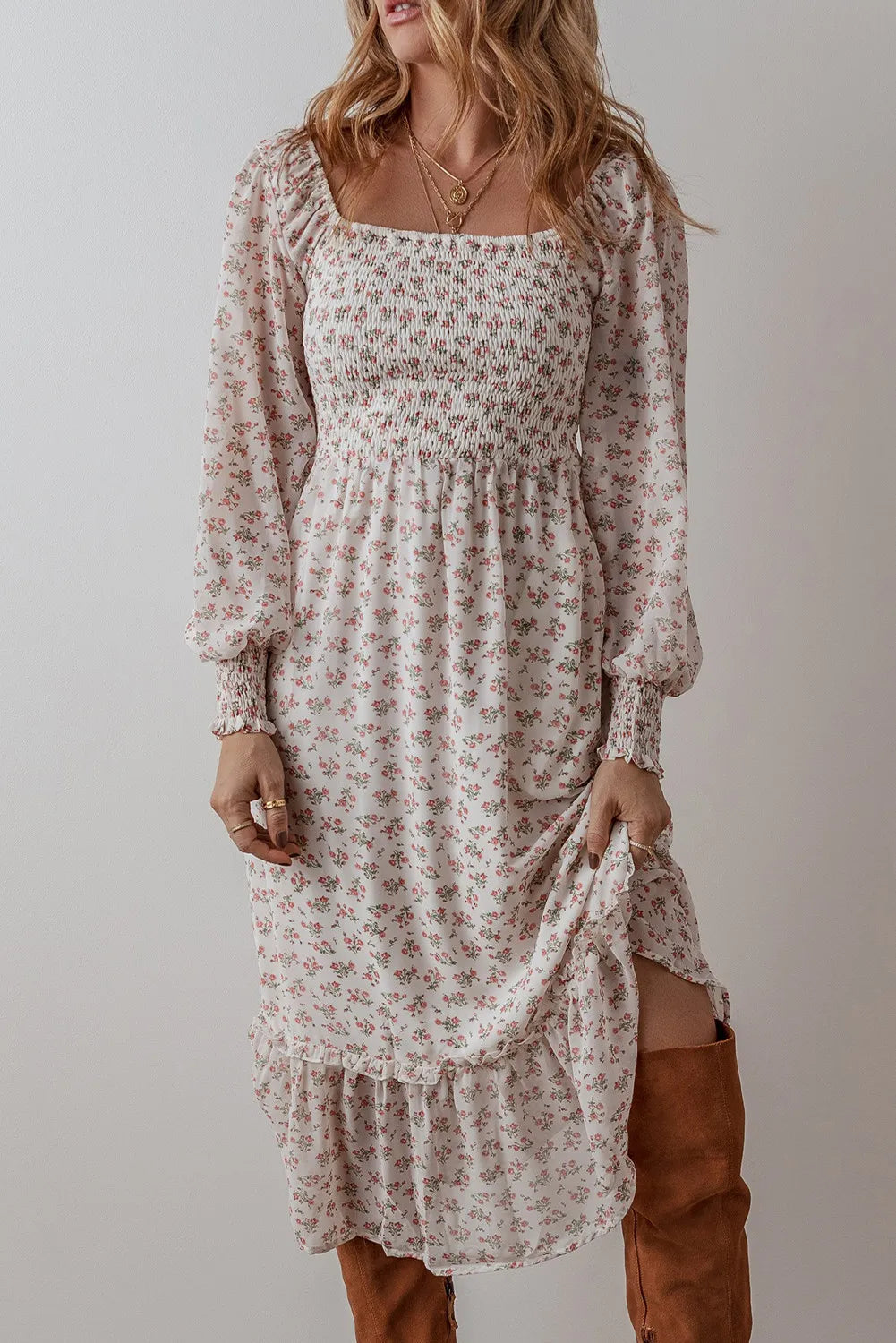 Smocked floral square neck long sleeve midi dress in white with small pink flowers, worn by a woman with long blonde hair, paired with knee-high brown boots.