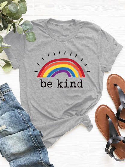 Gray "Be Kind" graphic t-shirt with rainbow design laid flat next to jeans and sandals.