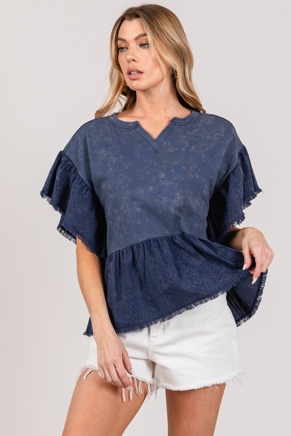 Woman wearing a blue ruffle sleeve washed short sleeve blouse paired with white shorts.