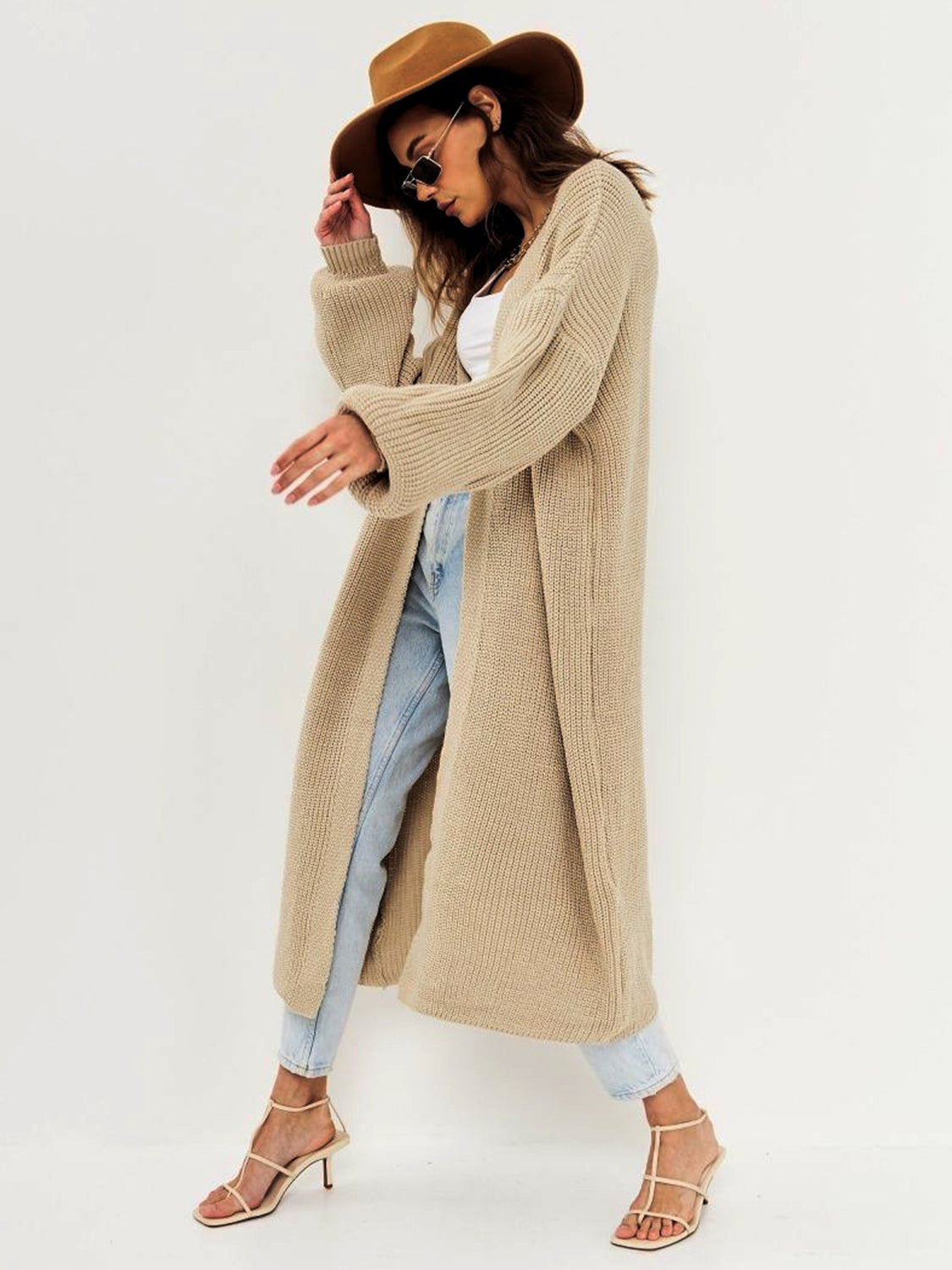 Open front long sleeve longline cardigan in beige knit fabric, styled with light jeans and a hat.