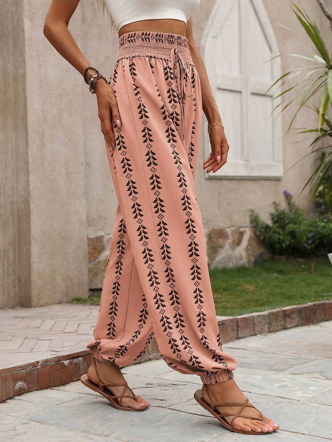 Tied printed high waist pants in pink with leaf pattern, made of 100% polyester, worn with sandals.