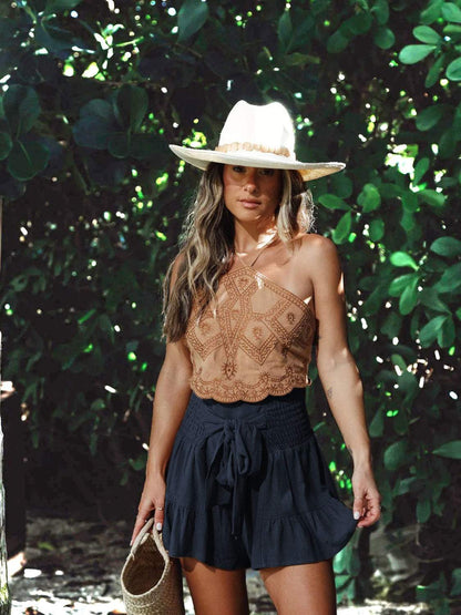 Woman wearing boho ruffled high waist flowy shorts with a tan top and straw hat, standing outdoors.