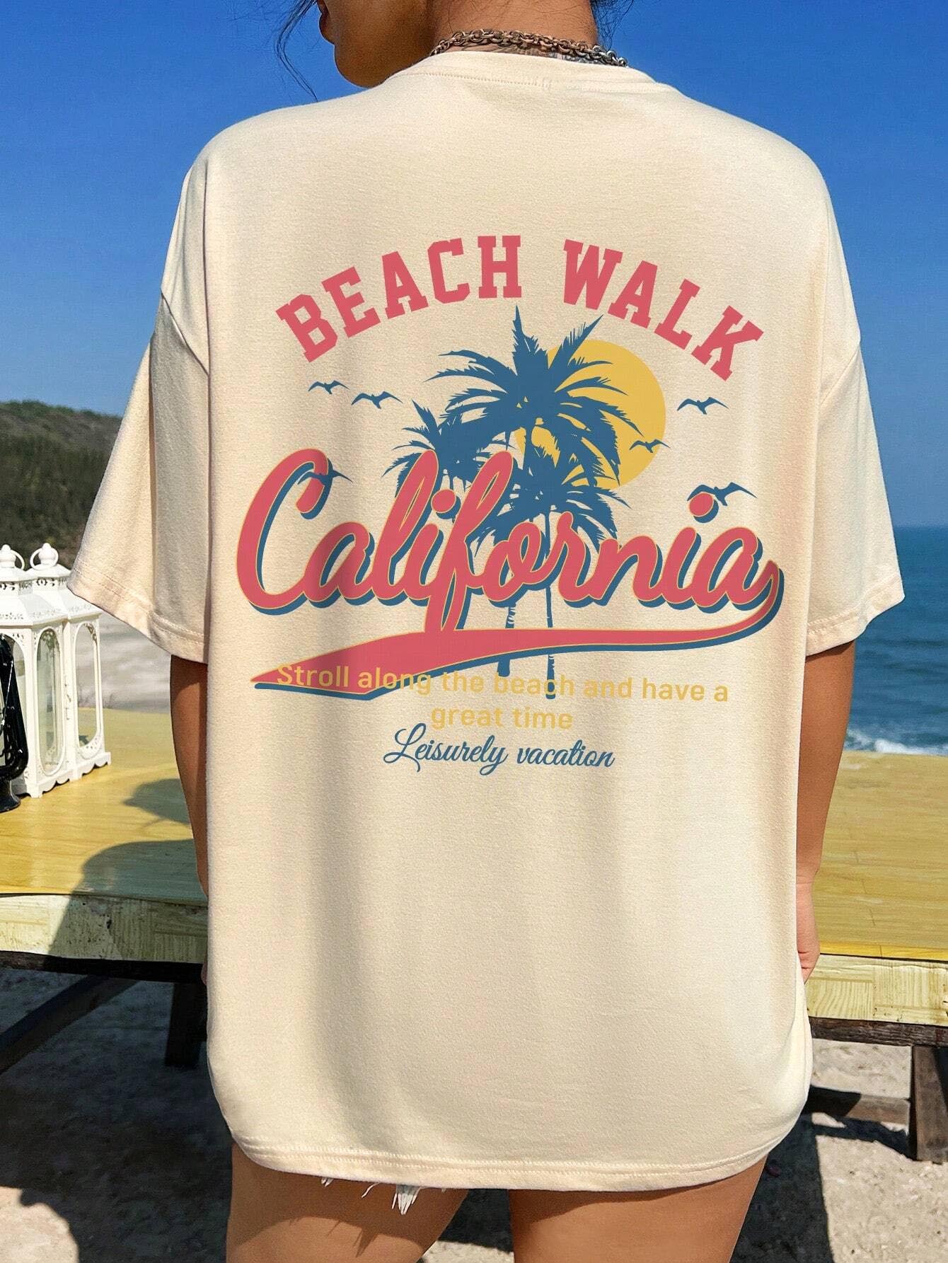 Beach Walk California Graphic T-Shirt with palm design on beige background, ocean in the distance.